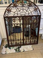 Front view of the closed wrought iron mirror showing the intricate arched top and fleur-de-lis ironwork on doors.