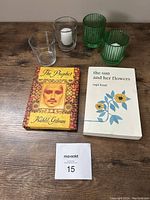Top-down image showing two paperback books (The Prophet and The Sun and Her Flowers) alongside four glass candle holders (two green ribbed glass, two clear smooth glass) with two white votive candles inside clear holders.