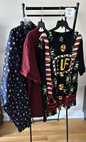 Photo of three men's tops hung on a rack showing a navy blue Christmas pattern top, a burgundy Canada T-shirt, and a candy-cane striped Christmas elf top.