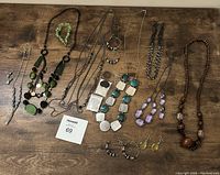 Photo showing assortment of costume jewelry including necklaces, bracelet, and earrings laid on a wooden surface.