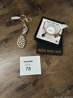 Top-down photo of the colorful peacock keychain featuring faux pearl tail and a boxed Alex and Ani bracelet with charms