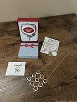Photo of the music charm bracelet displayed inside a gift box, kindness Earth Angel bracelet on card, and the silver necklace with geometric pendant laid side by side on wooden surface.