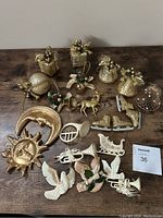 Top view of assorted gold holiday ornaments including fruits, birds, musical horns, sun, moon, horse, sleigh, dove, nativity figures, and a small bird cage displayed on a wooden surface.