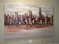 Framed acrylic painting showing an abstract city skyline with reflective water below, hanging on a wall.