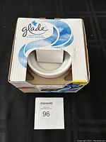 Front view of the Glade electric wax warmer in original cardboard box showing the top white ceramic dish and partially opened packaging.