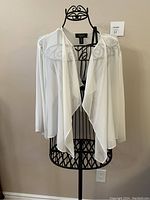 Ivory sheer cover top displayed open on black decorative mannequin, showing draped front and long sleeves.