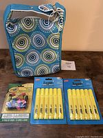 Photo showing front view of the blue insulated lunch bag with circular pattern, two packs of yellow Hype! highlighters and one pack of Crayola pencil-top erasers beside it