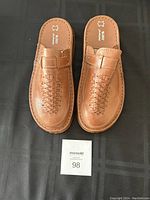 Top view showing the overall design of the brown leather sandals with woven pattern and buckle strip detail. Marked 100% natural leather on insole.