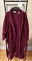 Front view of a men's burgundy terrycloth robe with shawl collar, two front pockets, and belt tie. Hanging on a black hanger.
