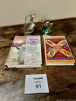 Two glass angel figurines with a journal and an audio cassette book set on a wooden surface.