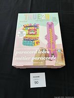 Front of the boxed TRUE2U Glow-in-the-Dark Paracord Loom Bracelet Making Kit showing colorful bracelets and the pink loom tool inside plastic packaging.