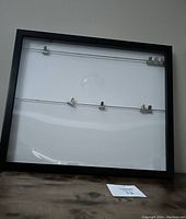 Full view of black picture frame with two metal wires and four clips inside.
