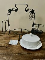 Full view of black metal serving stand with grapevine design, three detachable parts and white ceramic brie warmer with lid