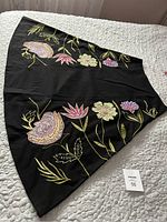 Photo of black skirt laid flat showing front embroidery of colorful flowers and sequins.