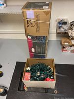 Photo showing two stacked boxed Christmas tree sets and a box containing coiled Christmas lights on the floor.