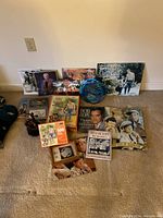 Photo showing the full collection including books, photos, puzzles, autograph sheets, and memorabilia in a casual arrangement on the floor against a wall