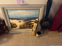 Wide shot showing all four items together: framed beach painting, brass matchstick holder with matches, wooden nautical bellows, and nightlight candle on carpet.