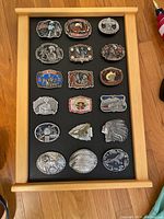Wooden frame displaying 18 metal belt buckles on black mat