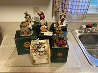 View of all seven Boyds Bears figurines displayed on a kitchen counter with four original green boxes and one cream-colored box visible.