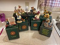 Seven Boyds Bears figurines displayed on their respective original green boxes on a kitchen counter.