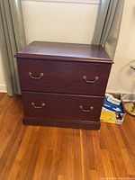 Front view of cherry wood filing cabinet with closed drawers showing brass handles and polished surface.