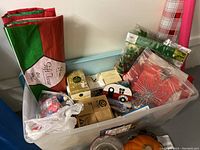 Plastic bin filled with various Christmas decorations including wrapping paper and boxed ornaments.