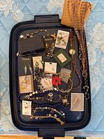 Full overview of costume jewelry lot laid on black tray including necklaces, bracelets, earrings, pins with various colors and styles