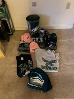 Lot layout showing all items including shirts, hats, throw blanket, trash can, cup, and keychains with Eagles logo prominently displayed.