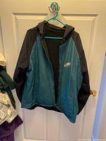 Front view of reversible Philadelphia Eagles jacket hanging on door. Green front with black sleeves and a hood. Eagles logo embroidered on chest.