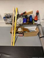 General view of the lot showing hand tools, ropes, cordless drill and flashlights on a shelf above boxes on the floor.