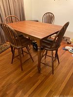 Rectangular solid wood high top dining table with four matching chairs in a room with hardwood floors.
