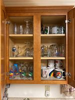Full view of the cabinet with all glassware and mugs visible on shelves, including stemmed wine glasses, shot glasses, and various mugs