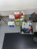 Photo of assorted solvent and bug control containers on a floor with basket containing brushes and gloves