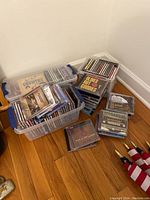 Photo of three plastic storage bins containing numerous country and other genre music CDs stacked and loose on the floor in a corner.