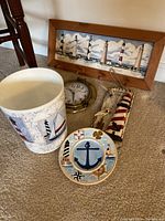 Photo of all nautical-themed items together on carpet: garbage can, round plate, brass porthole clock, lighthouse wall hanging, and coat holder