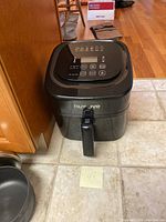 Closed view of the black Nuwave air fryer on tiled floor with the front handle visible.