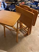 Three oak tray tables: two folded and standing together, one open and standing on legs.