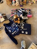 Full lot showing tank top, chair pad, two plush bears, Penn State scarf and hat, Barbie dolls in boxes.
