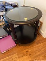 Side angled view of the round dark cherry side table with glass protector showing the full table and bottom shelf.