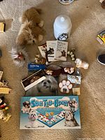 Overview of all Shih Tzu themed items on carpet including books, cookie jar, figurines, paw-shaped item, and board game.