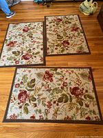 Three rectangular area rugs with beige background and floral print in red, green, yellow, and brown border on hardwood floor.