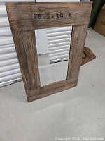 Full view of the framed mirror showing the rustic barnwood style brown frame and the central reflective mirror surface with dimension 28.5 x 39.5 inches marked on top frame.
