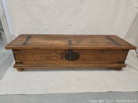 Front view of the antique wooden blanket chest showing distressed wood and patinated metal hardware on the lid and front panel.