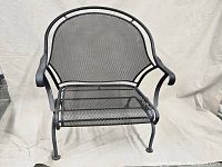 Front view of coil spring patio chair showing mesh seat and backrest, and scrolled metal arms.