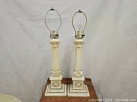 Pair of Hollywood Regency style column lamps without shades, showing cream and gold distressed finish and classical details.