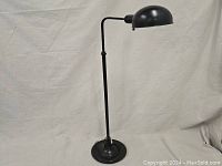 Full view of industrial style floor lamp with adjustable arm and rounded weighted base, black finish.