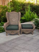 Image showing large wingback lounge chair and matching stool placed outdoors on a tiled patio with plants in the background.