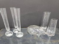 Photo showing three tall fluted stem vases with round controlled bubble glass bases, clear glass piggy bank in pig shape, and two small weighted bottom vases.