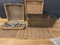 Full lot with four woven baskets arranged vertically behind two rectangular placemats laid flat and one basket holding flatware in front.