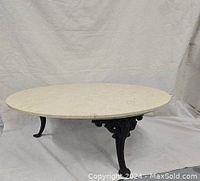 Front view showing the round natural marble top and detailed wrought iron base with three legs.